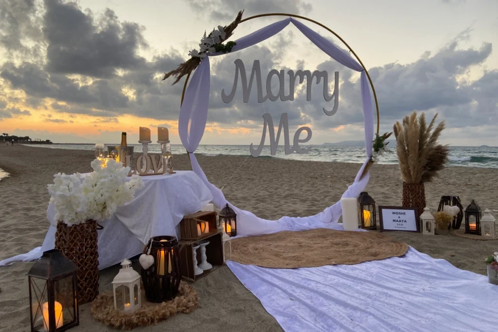 Boho style marriage proposal setup on a Crete beach at sunset with soft decor