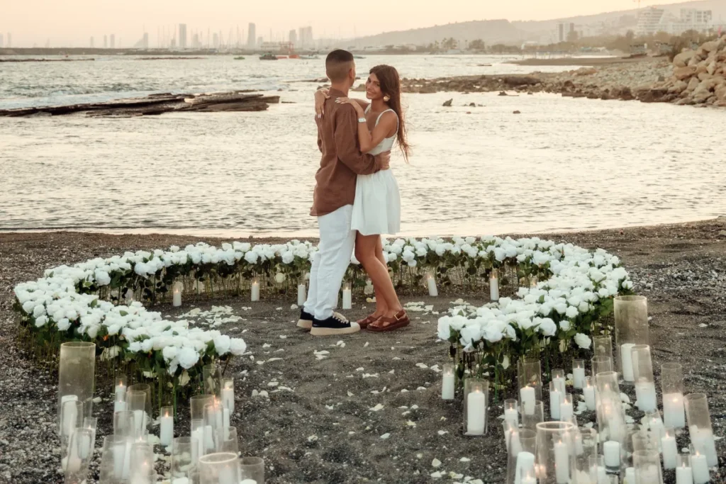 Couple celebrating their marriage proposal on a beach in Cyprus with a luxury floral heart, candles and romantic sunset setup.